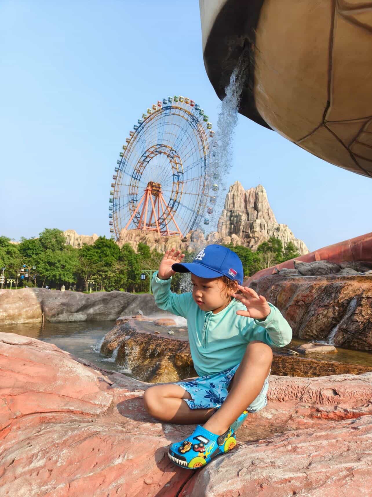 Child posing in front of giant ferris wheel at VinWonders Phu Quoc theme park