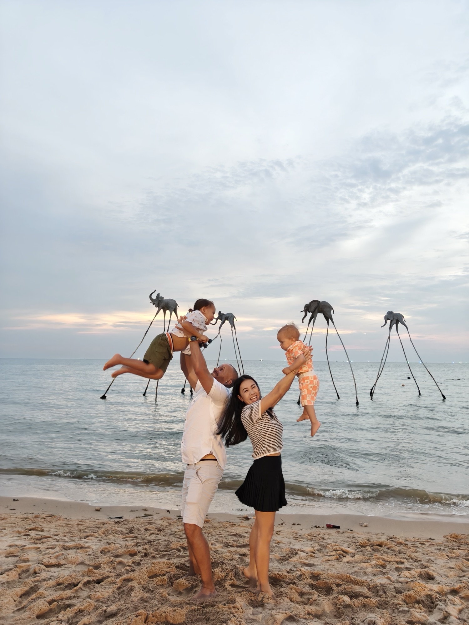 Family with kids standing between two giant stone face statues on the sand in Phu Quoc Vietnam