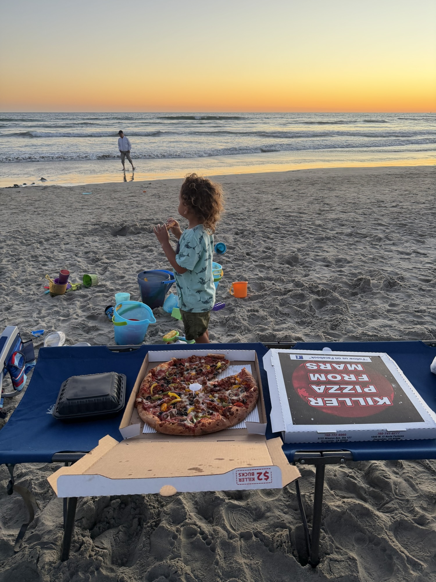 Pizza boxes on a folding table set up directly on Oceanside beach at sunset