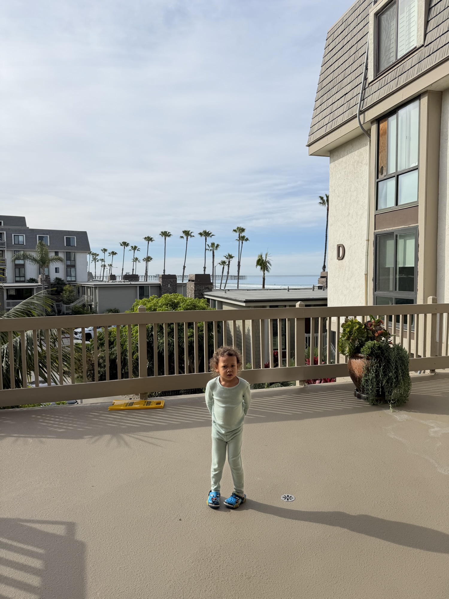 Child standing on condo balcony with a view of Oceanside beach and palm trees