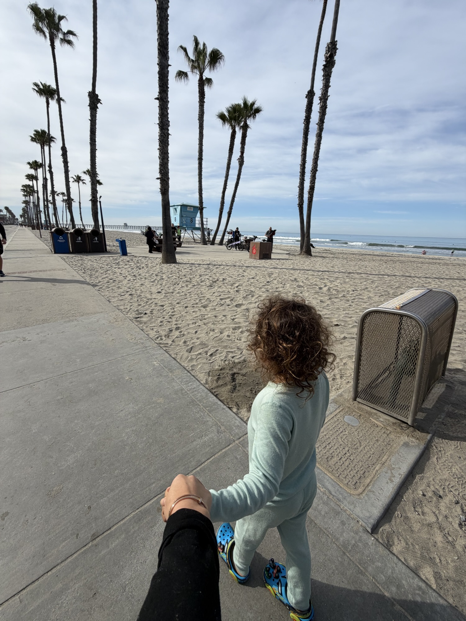 Parent holding a child’s hand walking along the Oceanside beachfront path in the morning