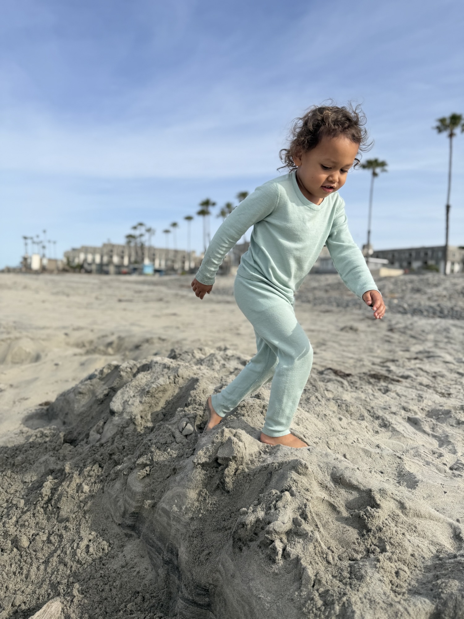 Child in pajamas climbing on a small sand mound on Oceanside beach