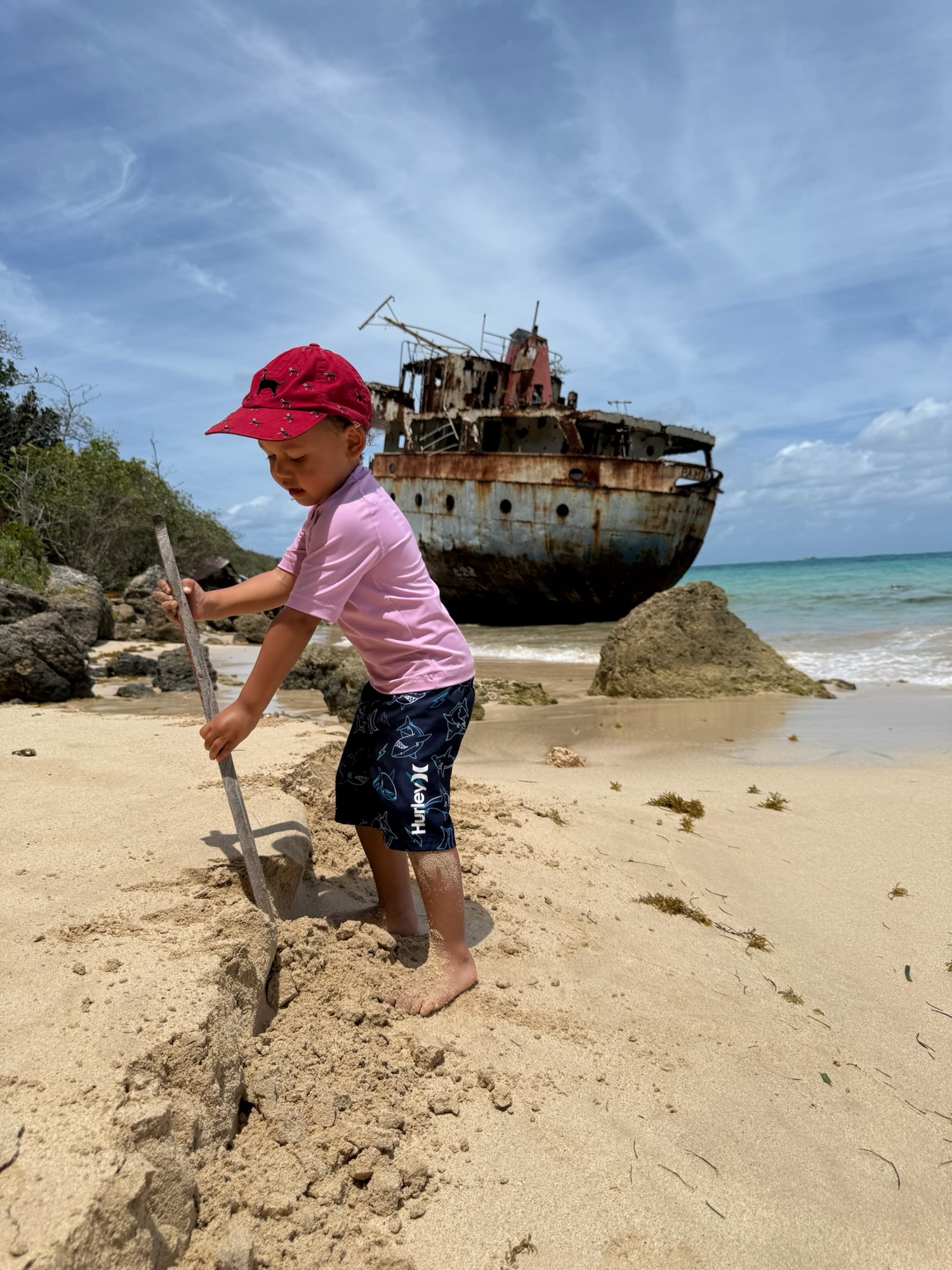 Child digging in the sand near a rusted shipwreck on a secluded Anguilla beach