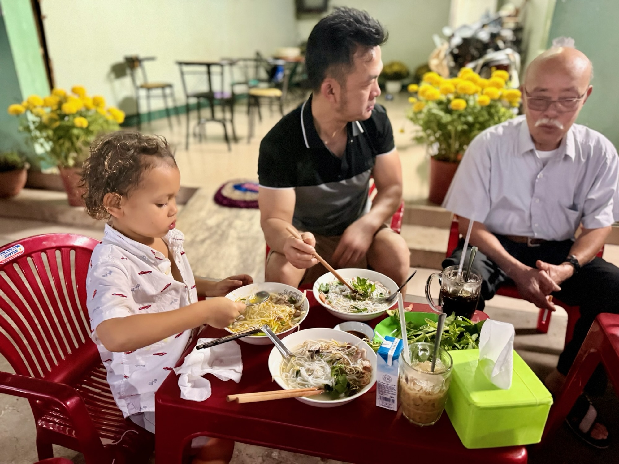 Young child eating a bowl of Vietnamese pho for breakfast at a local market at dawn