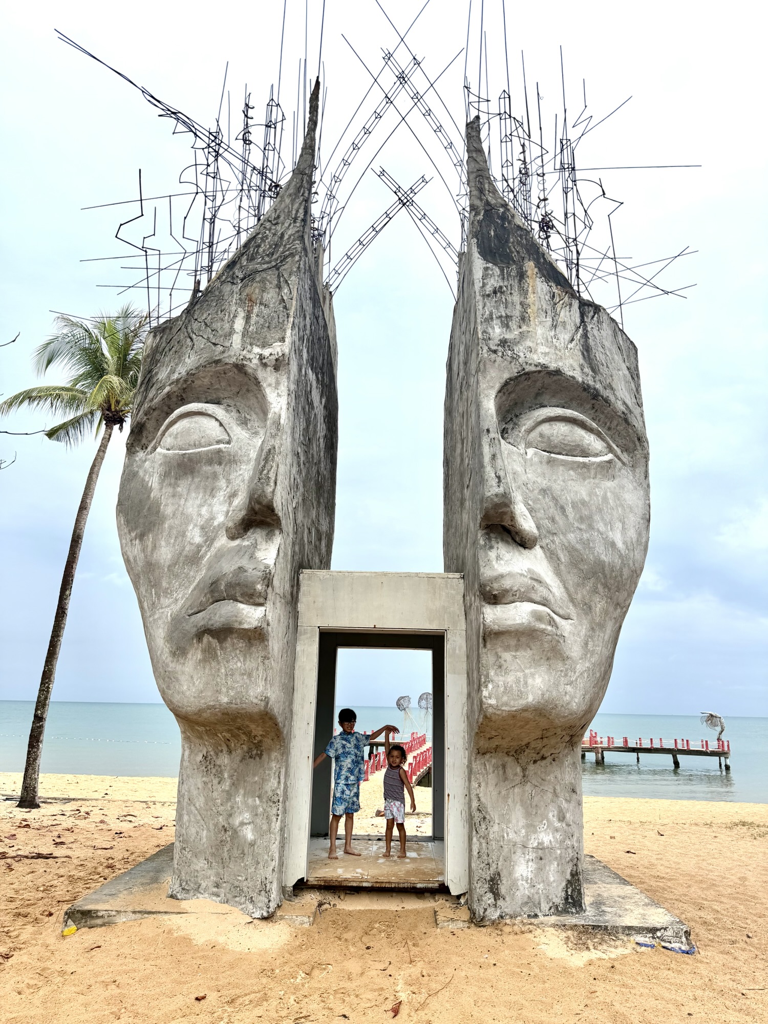 Mom lifting child near a metal tree sculpture on the beach in Phu Quoc Vietnam